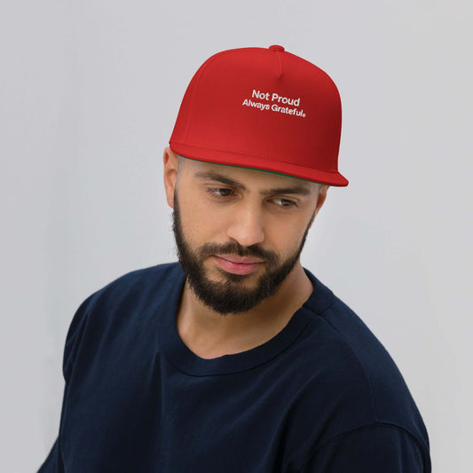 A man wearing a red Flat Bill Cap with the message 'Not Proud Always Grateful.' in white embroidery.